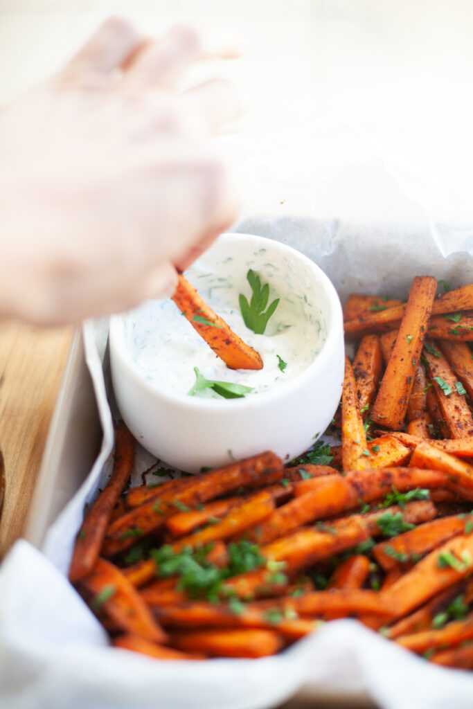 hand dipping into Spicy Carrot Fries with Lemon Cumin Yogurt Sauce | macro friendly sides recipe by www.lillieeatsandtellscom.bigscoots-staging.com
